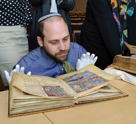 Adam Cohen wearing white gloves looking at an old book from the Middle Ages.